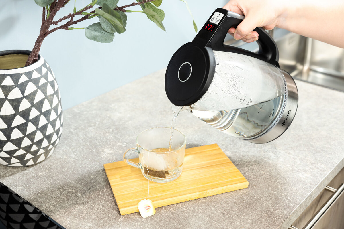 Person pouring water from the kettle to a tea cup