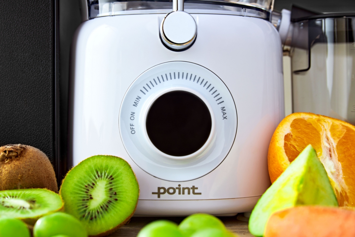 A close-up picture of a white Point juicer's front panel with a black roating knob and a lit-up panel with orange and green fruits around the device