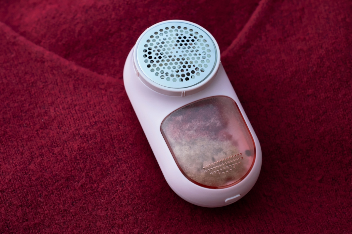 A pink Point lint remover on top of a red sweater with its see-through tank full of lint from the sweater