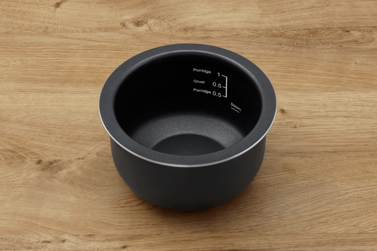 The black-colored inner pot of the Point rice cooker on a wooden table with its measuring scale showing inside the pot