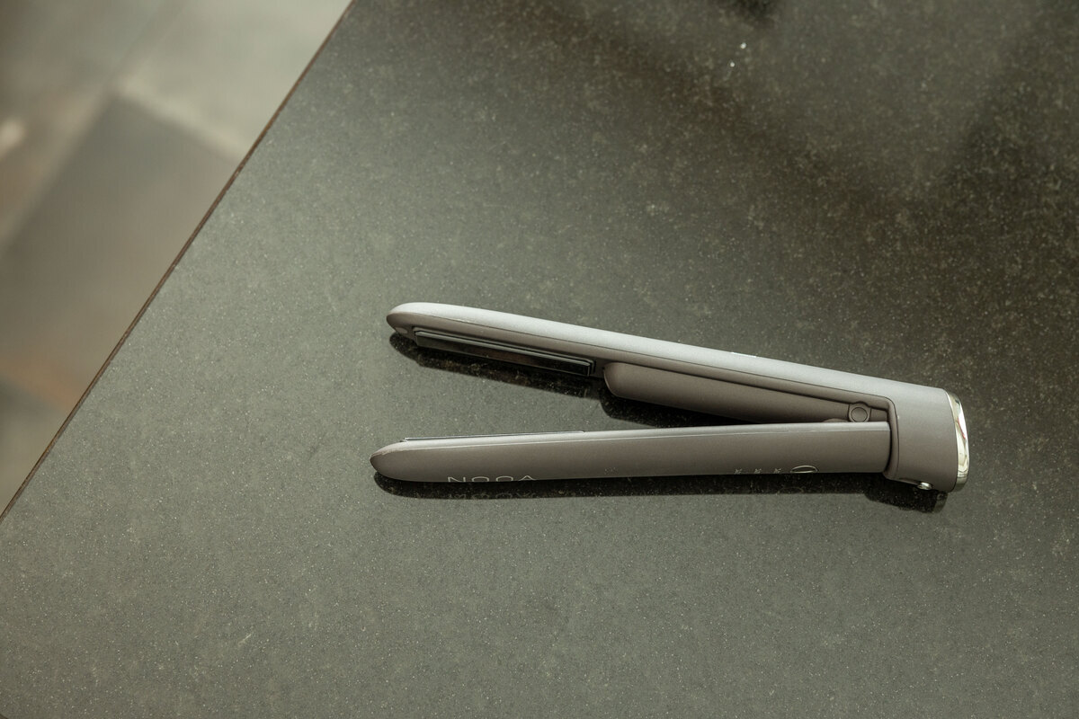 A close-up picture of a dark grey NOOA straightener on a shiny dark kitchen table