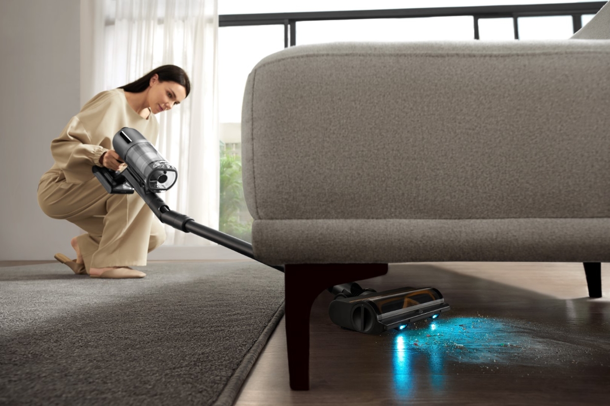 Person crouching to vacuum underneath a couch with the flexible DREAME Z30 STICK VACUUM CLEANER and its floor nozzle with blue lights