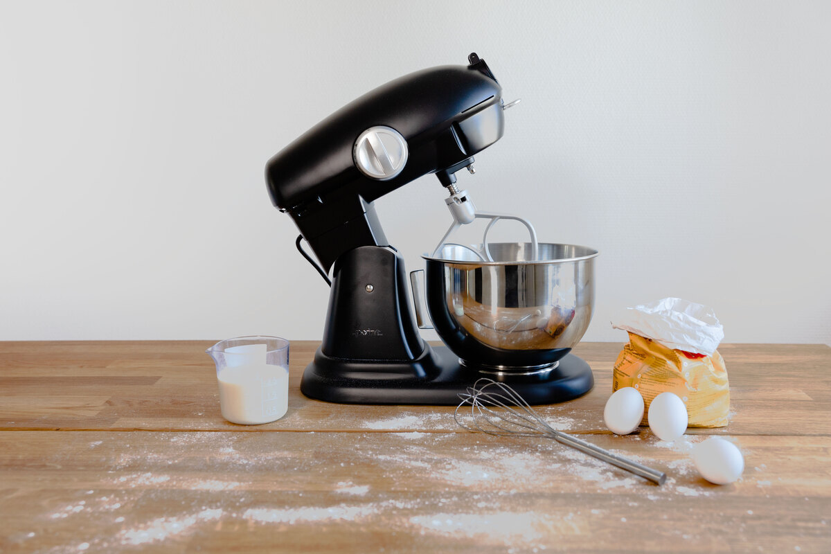 A picture of a black kitchen machine on a wooden table with flour and eggs