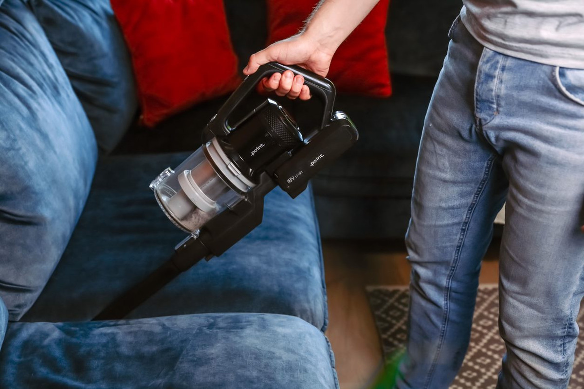 A close up of the handheld vacuum of the POINT POVC618DB 18V stick vacuum vacuuming from in between blue couch cushions