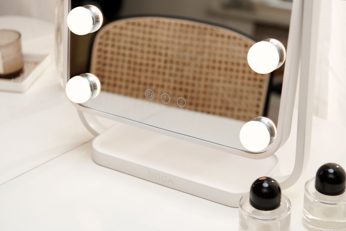 A close-up picture of a NOOA Glow Hollywood mirror with its light on and a few make-up bottles next to it on the table