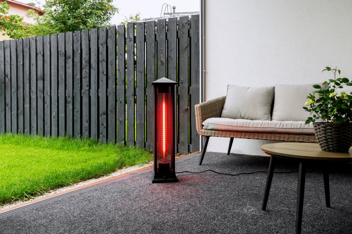 Wide angle image of the POINT PRO POPHTOW81 PATIO HEATER outside with green grass to the left and a comfy grey sofa behind the heater