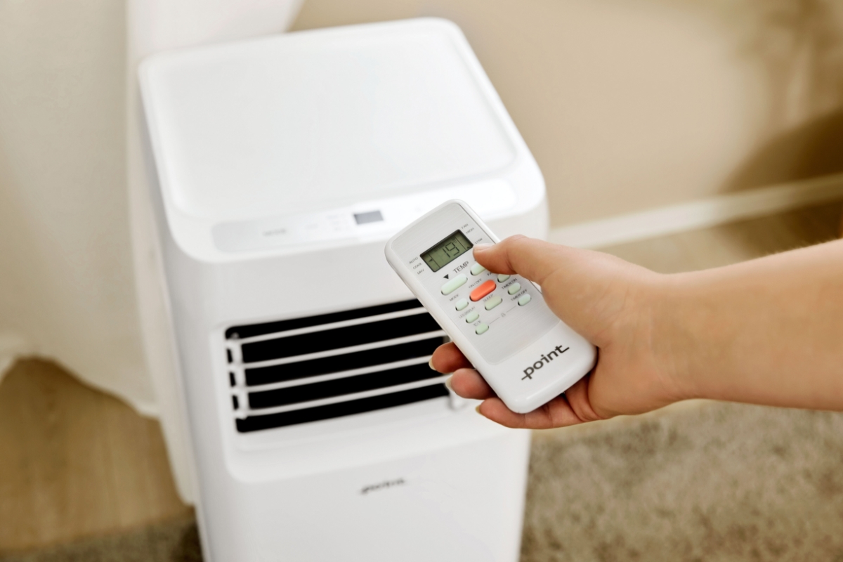 Close up of person using the remote control of the Point POAC7024 air conditioner