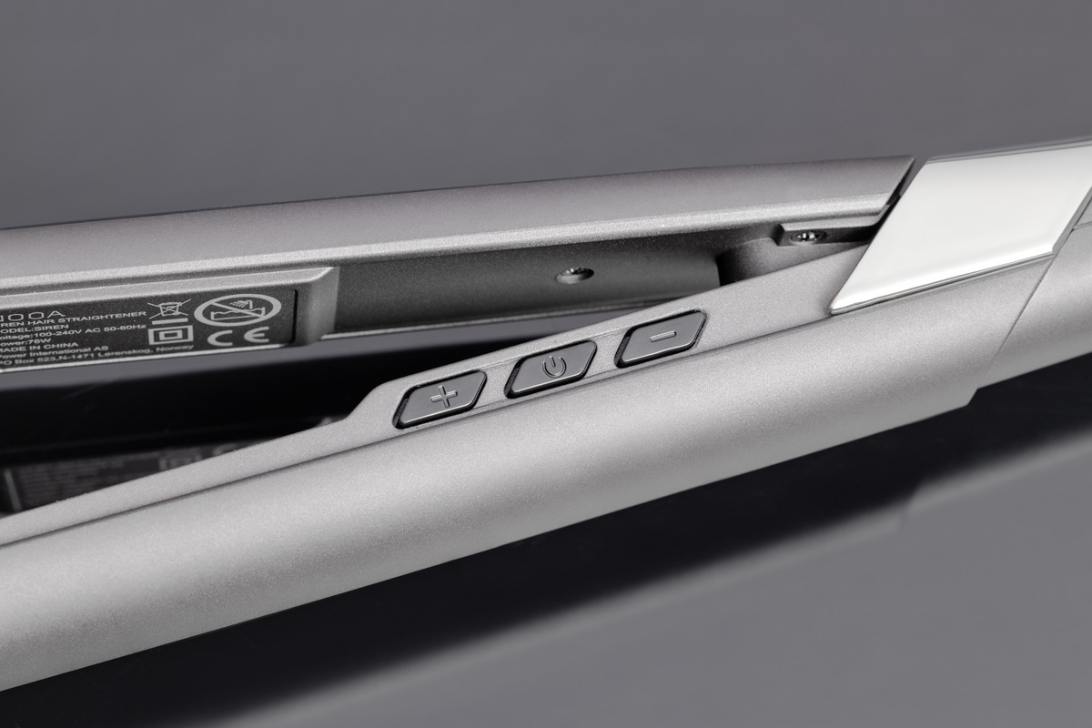 A close-up picture of NOOA matte grey hair straightener's handle with all the temperature settings and a shiny table under the straightener with a small reflection