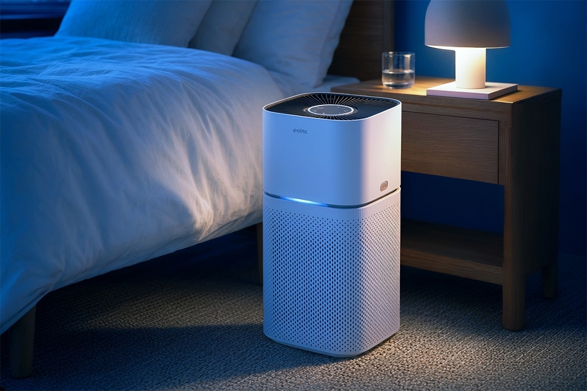 A white Point POAP350 air purifier in a dark bedroom next to a bed on the floor with a tiny night light behind the product and blue light coming out of the purifier