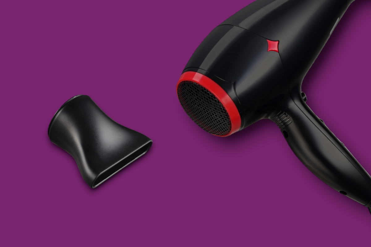 Studiobilde av en sort hårføner med en rød detaljring og et munnstykke mot en ensfarget lilla bakgrunn.