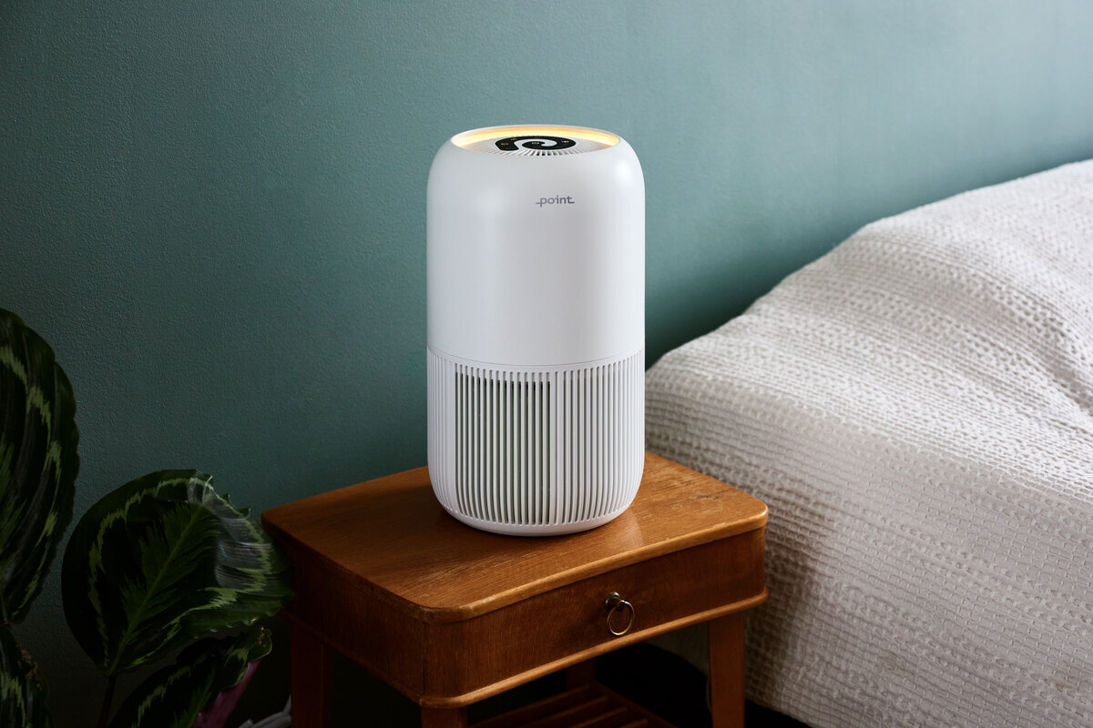 Air purifier on the side table next to a bed and plant