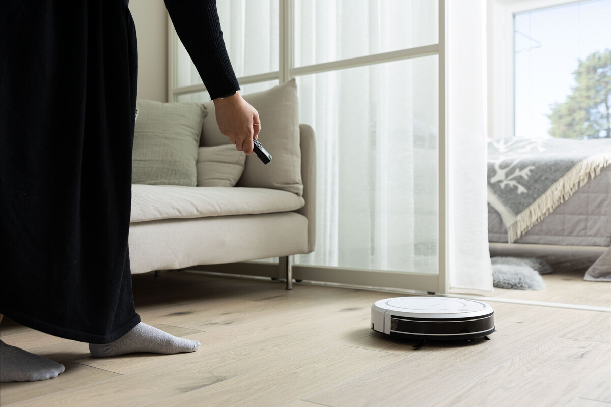 Woman adjusting robot vacuum cleaner with the remote control