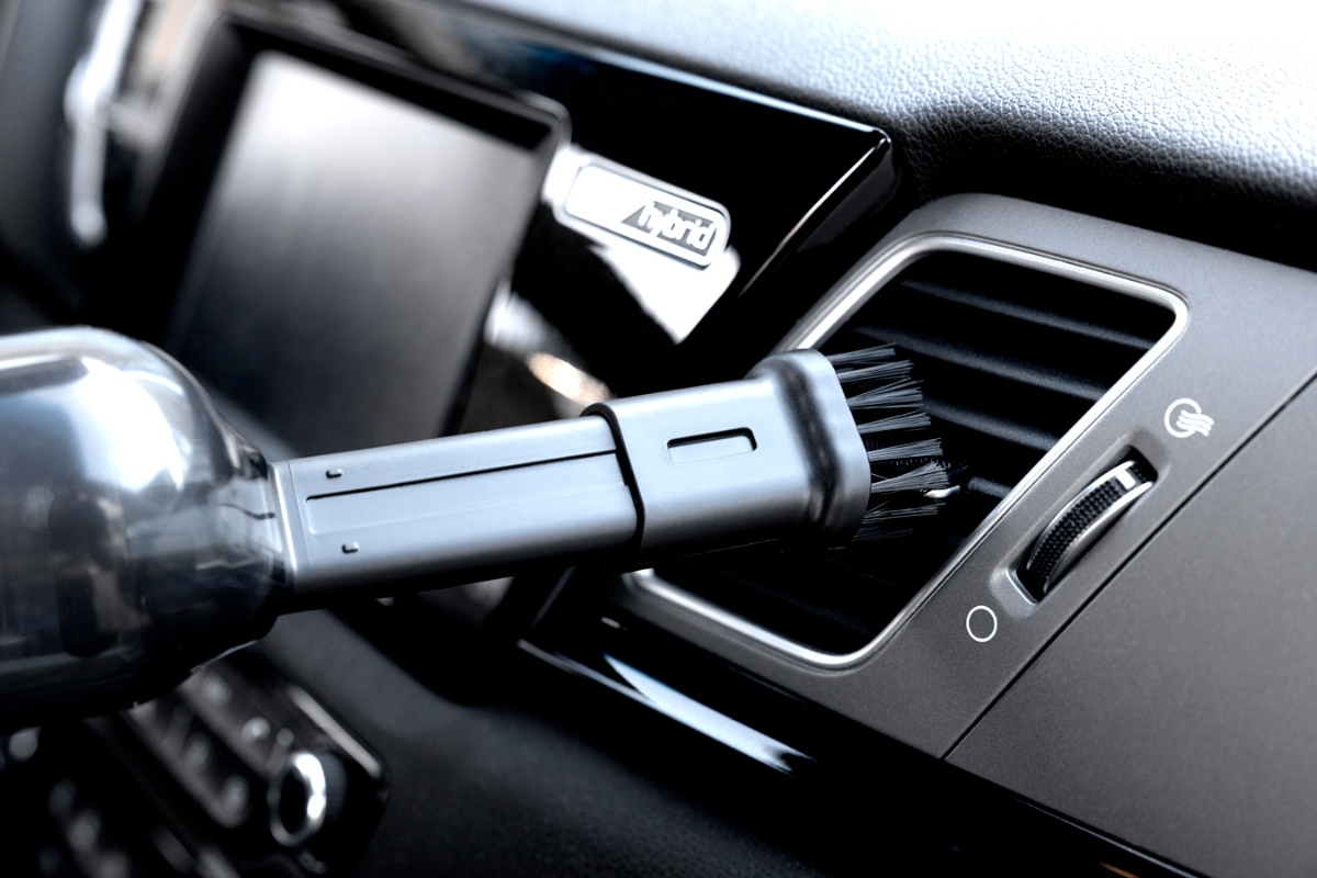 A black Point Tornado handheld vacuum cleaner being used in a car with its combination nozzle vacuuming a black air vent inside the car