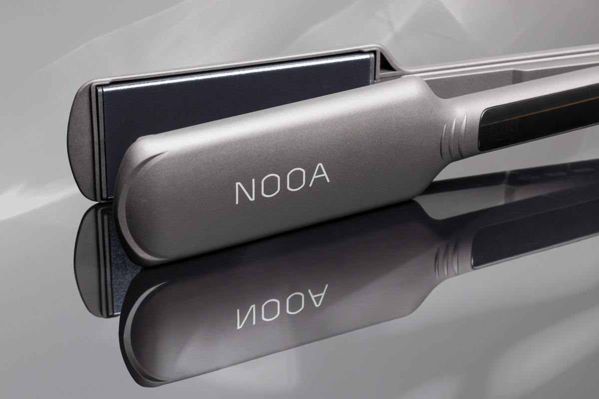 A close-up picture of NOOA matte grey hair straightener's wide straightening plates and the straightener placed on a shiny table with reflection