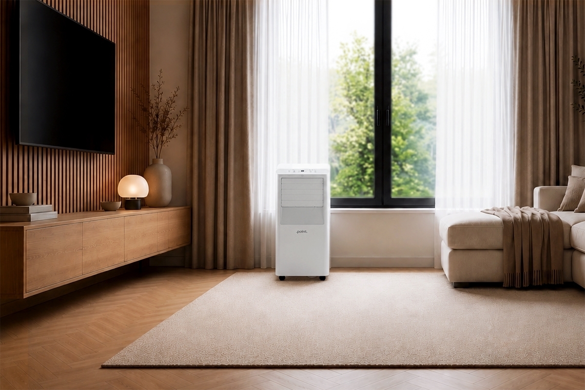 POINT POAC7K25 PORTABLE AC 7000BTU A white Point AC in a warm toned living room with lots of light and a beige sofa on the right side with the AC device in front of the window and lots of greenery outside