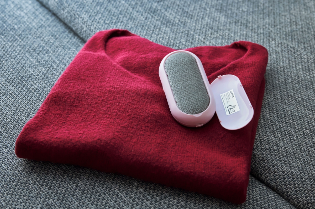 A pink Point lint remover on top of a red sweater with its back panel detached and a grey-colored lint brush showing