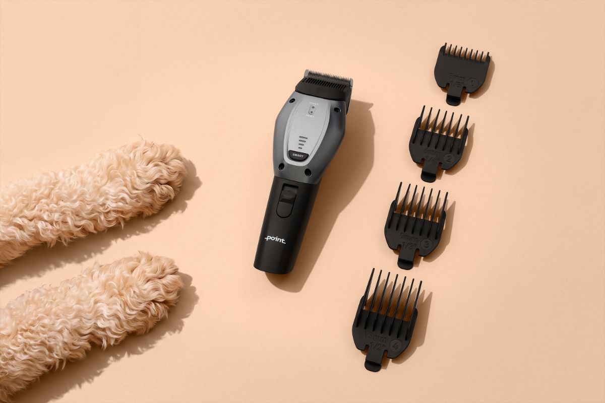 POINT PET GROOM PET TRIMMER A beige table with two paws of a light-brown dog with the silver Point Pet trimmer and the black guide combs on the table next to the paws