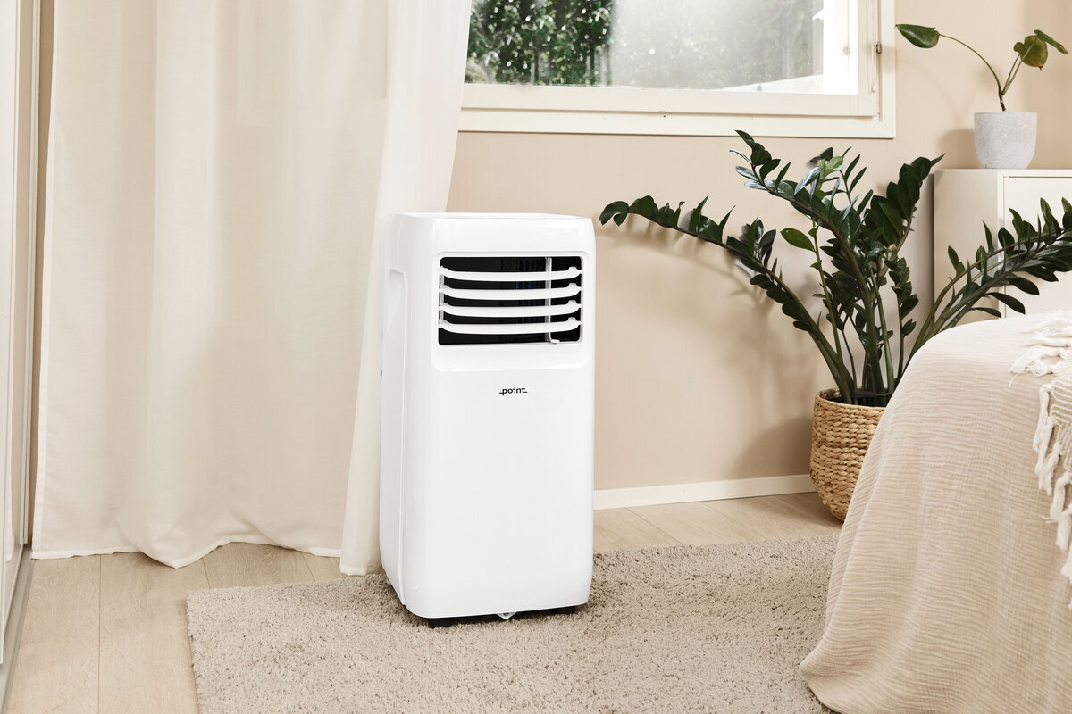 A wide angle picture of the POINT POAC6022 air conditioner in front of a beige wall with a green plant behind it next to the wall 