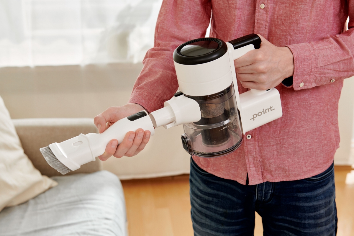 A medium shot of a person wearing a light red shirt detaching the furniture brush of the handheld version of the Point Pencil stick vacuum cleaner