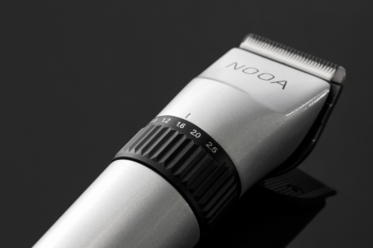 A close-up picture of a silver-colored NOOA hair Clipper and its adjusting ring and the device placed on a shiny black table