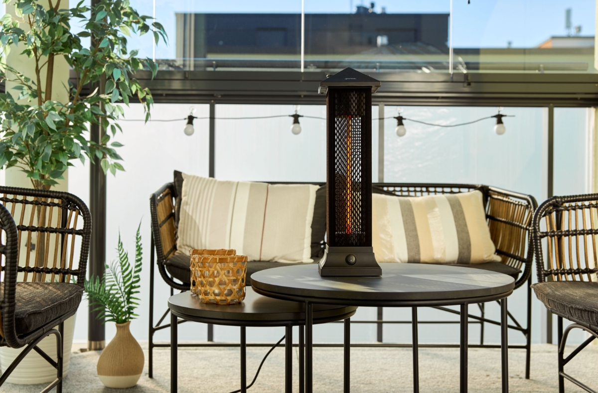 Wide shot of the POINT PRO POPHTOW53 patio heater on a coffee table on a sunny balcony with greenery and a light series hung on the handrail behind the heater