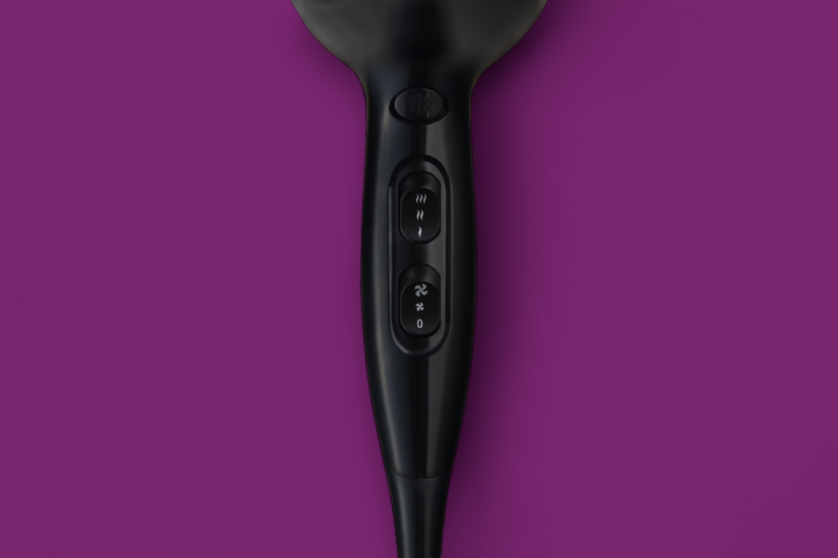 Nærbilde av en svart hårføner mot en lilla bakgrunn, som viser strøm- og hastighetsinnstillingene med tydelig synlige varme- og vifteikoner.