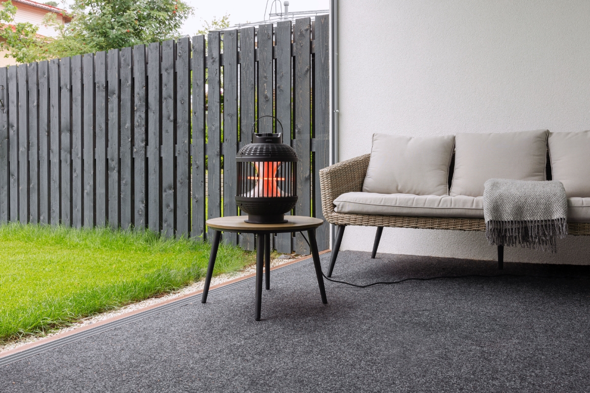 Wide angle image of POINT PRO POPHLAN47 PATIO HEATER on a table outdoors, with green grass to the right and a comfy grey sofa on the background