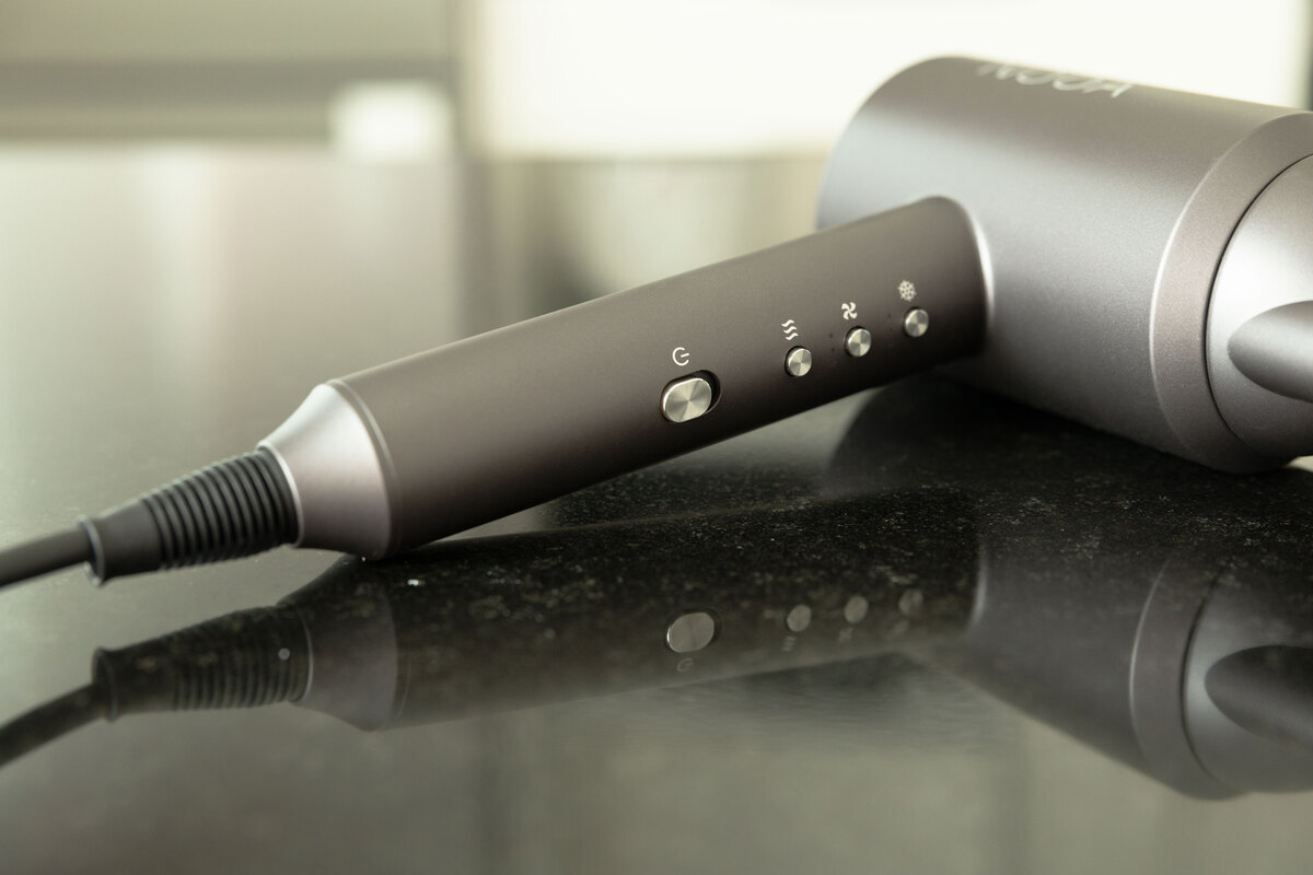 Close up of the NOOA LUXE BLDC hair dryer lying on a table, focus on the handle and its buttons