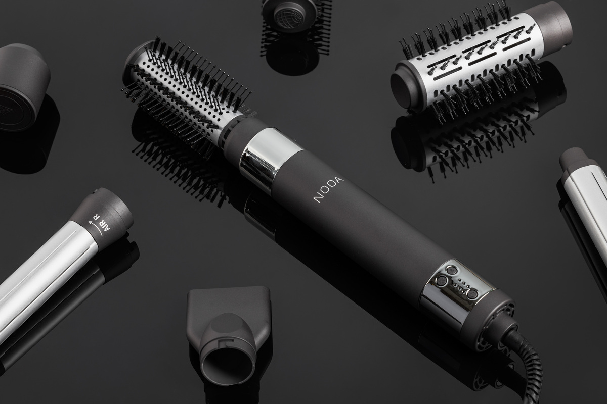 A black-colored NOOA Allure hot air styler placed on a black shiny table and with all its accessories surrounding it