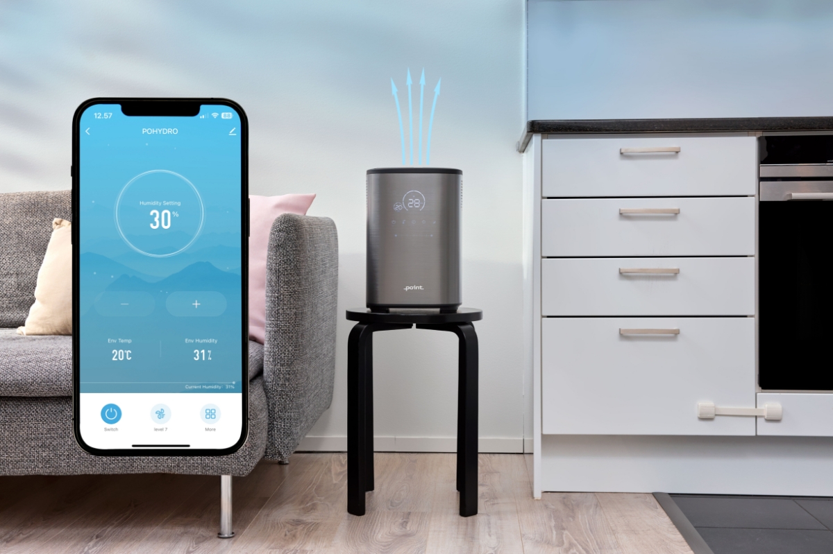 A picture of a Point Pro Hydro humidifier placed on a stool next to a grey couch and blue arrows point out of it showing the air vents and a big picture of smartphone showing the app