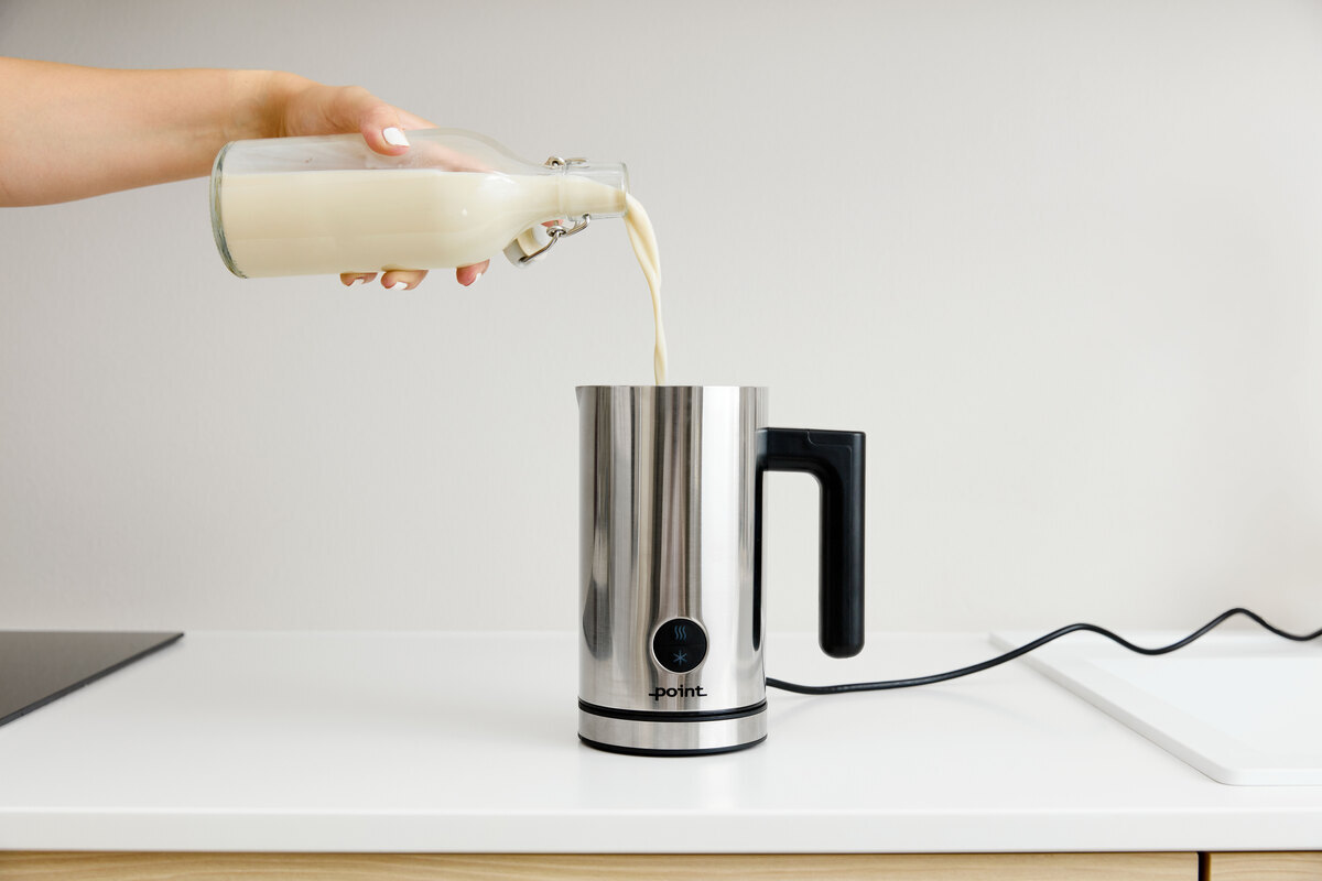 A person pouring milk from a glass jar into the POINT POMF17SS milk frother on a white kitchen counter