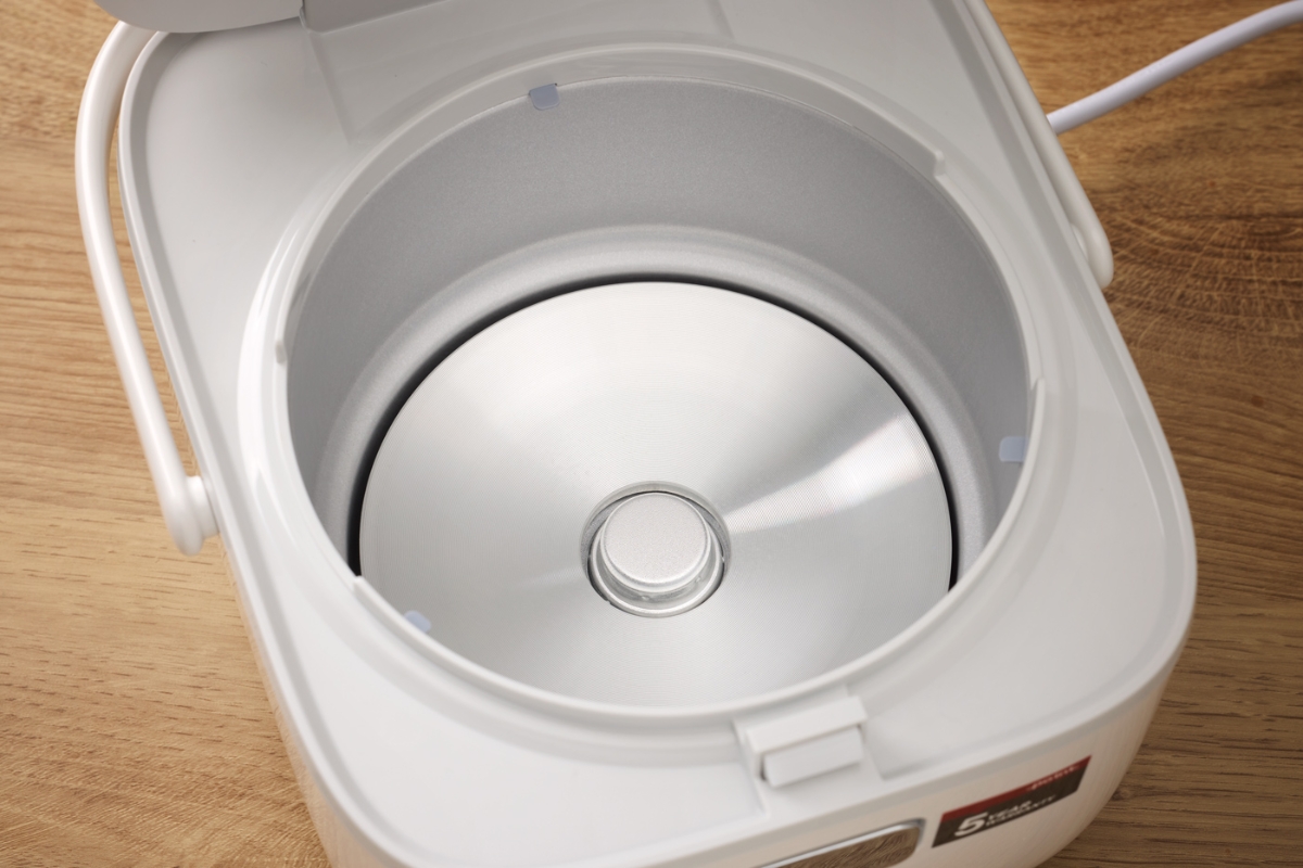 The silver colored interior of the white Point rice and multicooker pictured from above and the device on top of a wooden table
