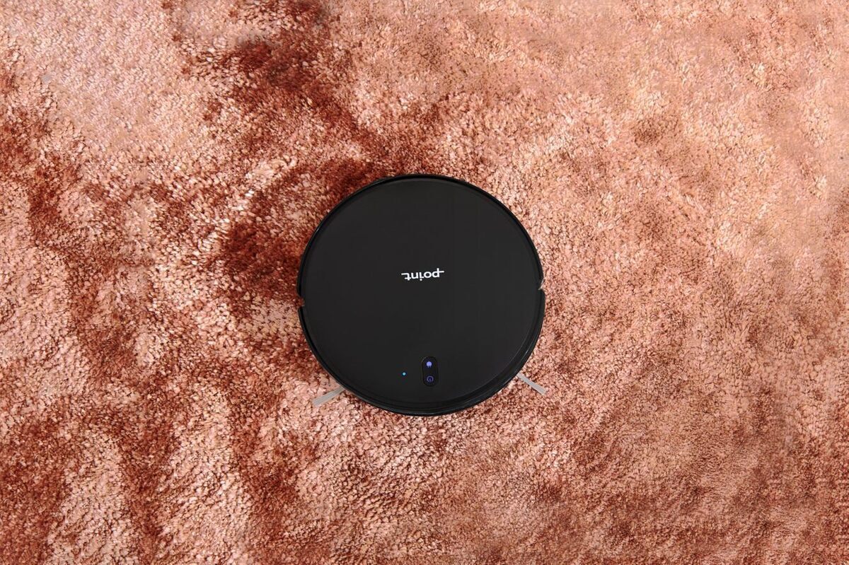 A picture of a black Point Dusty robot vacuum cleaner vacuuming a pink carpet