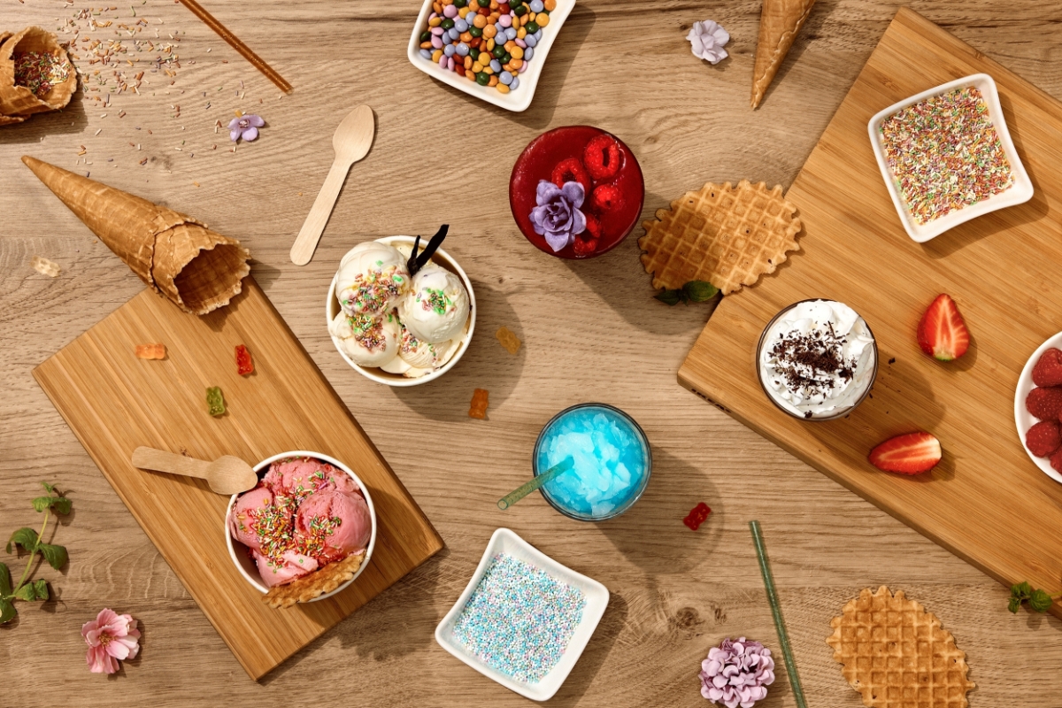 A wooden table filled with different frozen desserts on wooden cupboards and sprinkled with nonpareil, waffles and flowers