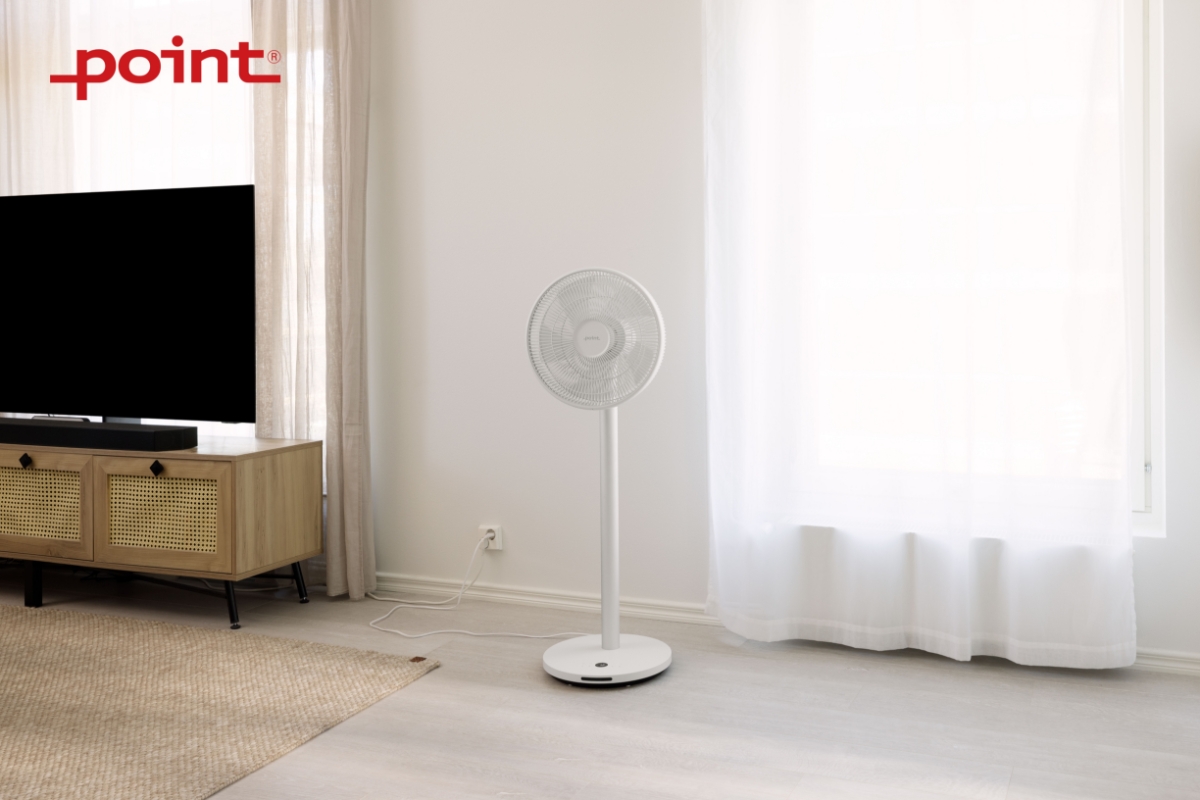 Wide angle image of POINT POFS16ALU 16" DC SILENT STAND FAN next to a TV console, in front of white curtains with sunlight shining through