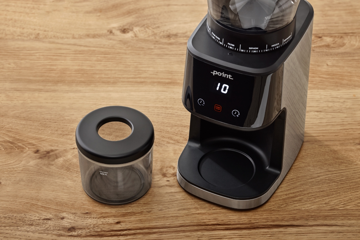 A black Point Pro coffee grinder on a wooden table with its screen showing with digital number and a coffee bean container attached and next to the device