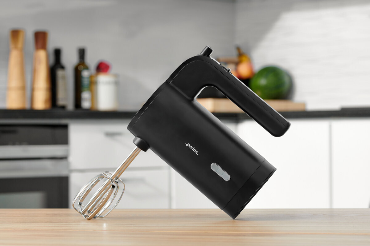 A picture of a black Point hand mixer standing on a wooden kitchen table with lots of light around it