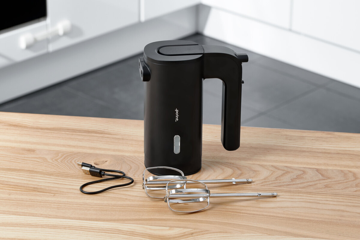 A picture of a black Point hand mixer standing on a wooden kitchen table with all its accessories next to it on the table