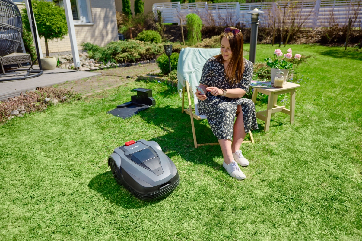 Woman enjoying summer in the sunbead, while robot vacuum cuts the lawn