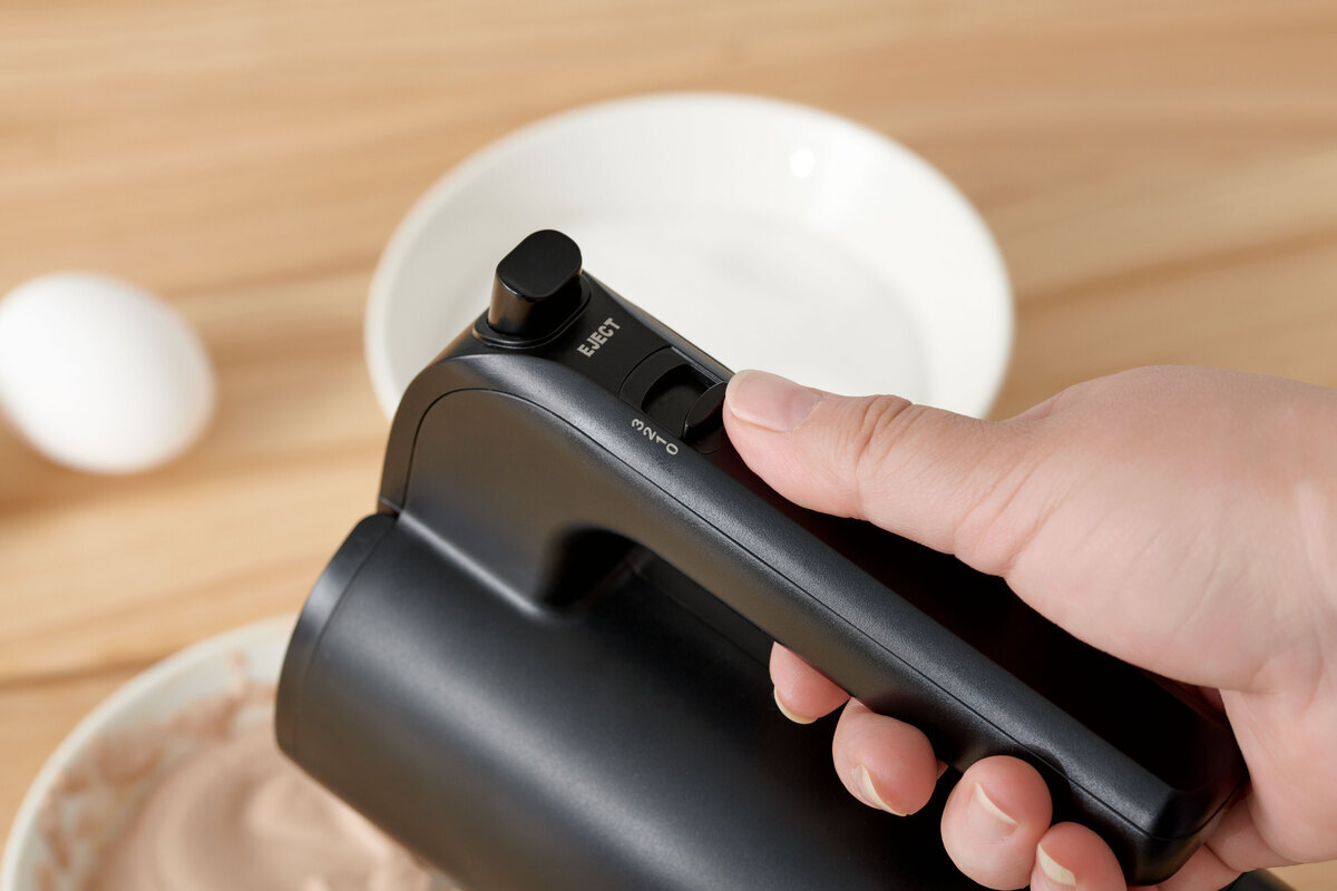 A close-up picture of a black Point hand mixer's handle held by a person who is whisking a dough