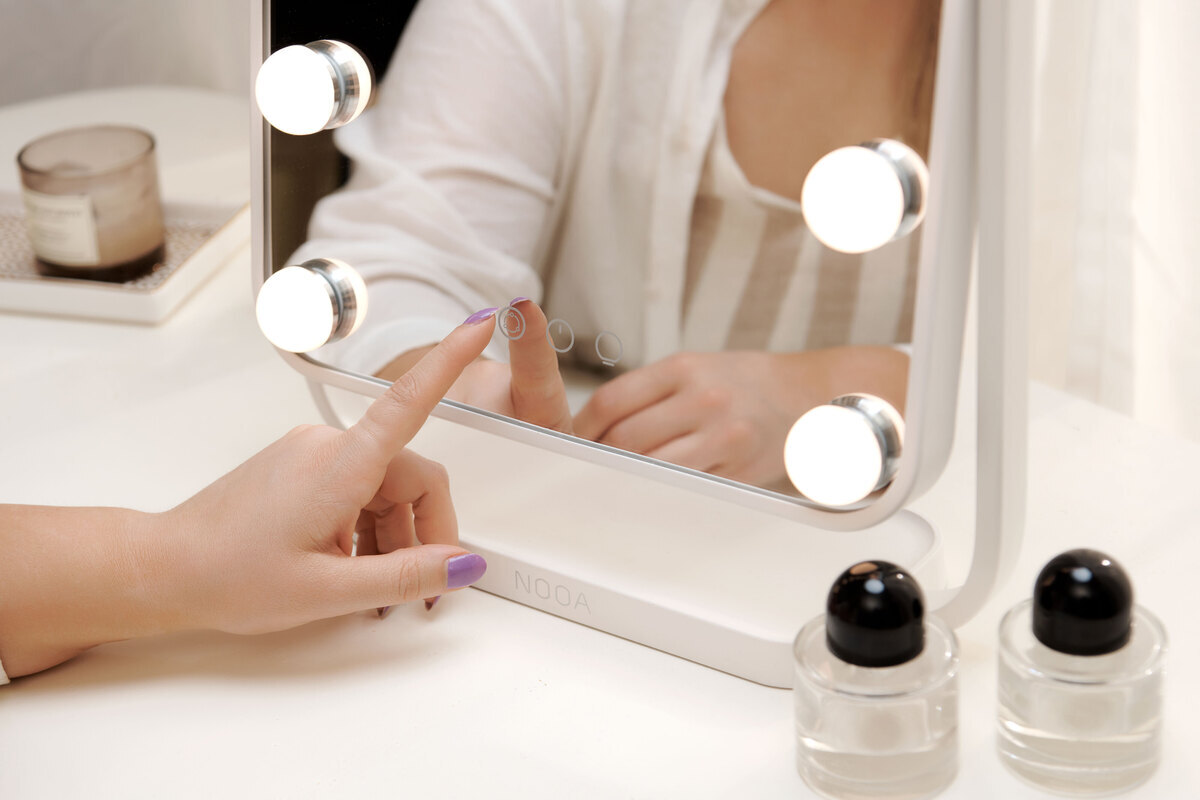 Woman's hand touching the NOOA makeup-mirrors touch buttons and the white bulbs of the mirror shining their light