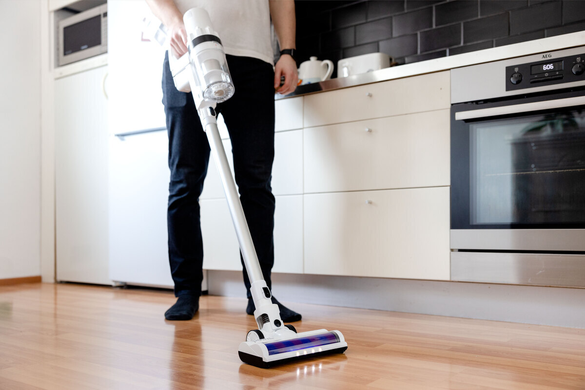 A man vacuuming a wooden floor of a kitchen with Point stick vacuum cleaner