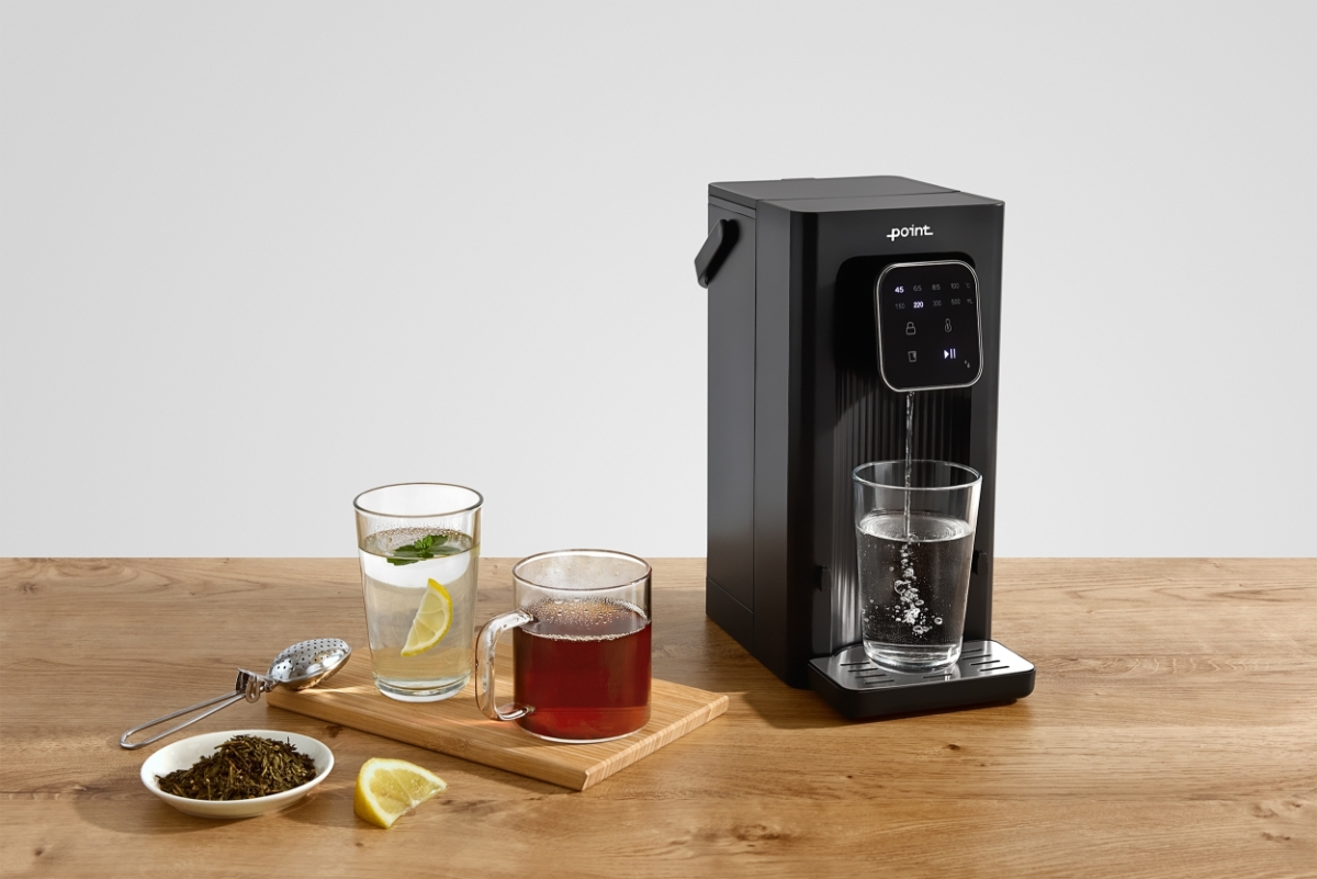 POINT POWD5000 INSTANT HOT WATER DISPENS A black Point hot water dispenser on a wooden table with a wooden chopboard next to it with two glasses of different color teas on top of the chopping board