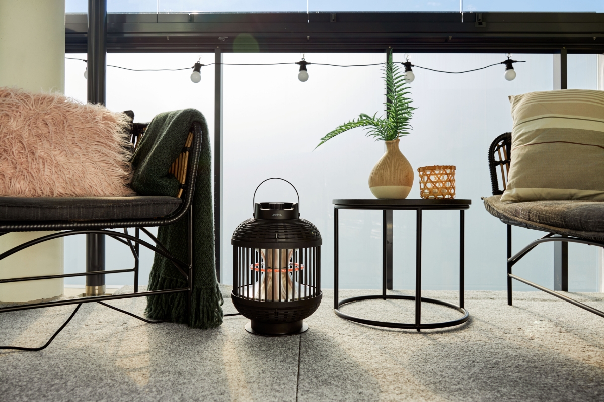 Wide image of POINT PRO POPHLAN47 patio heater on a sunny balcony. On both sides are lounge chairs with pillows and blankets on them. On the right of the lantern is a side table with a plant and a candle holder.