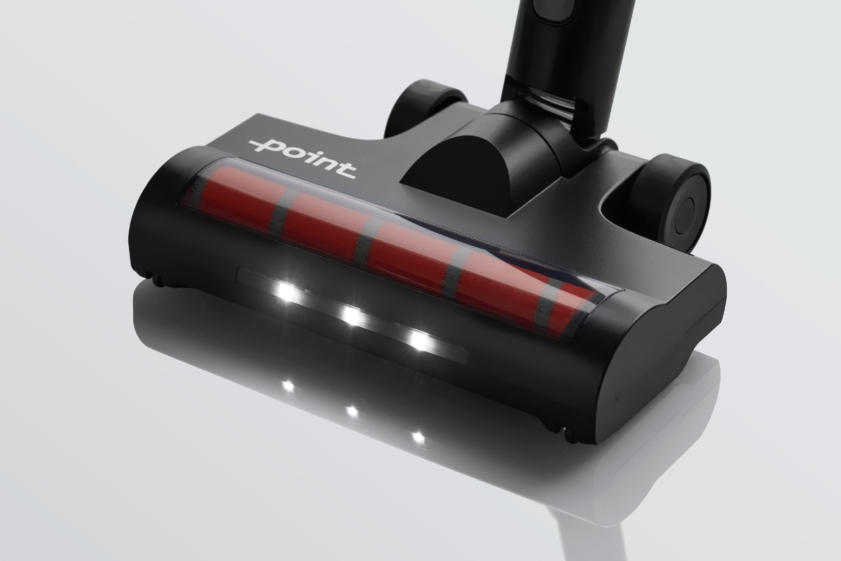 A black and red colored Point Cruise stick vacuum cleaner's floor brush up-close with its LED lights on and the nozzle on a shiny all-white floor