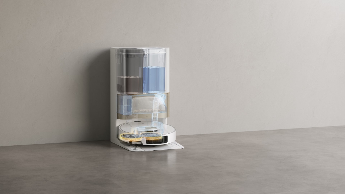 A white Dreame X40 Ultra robot vacuum cleaner on its cleaning station in an empty light-dark colored room with the station being transparent showing the cleaning functions of the station