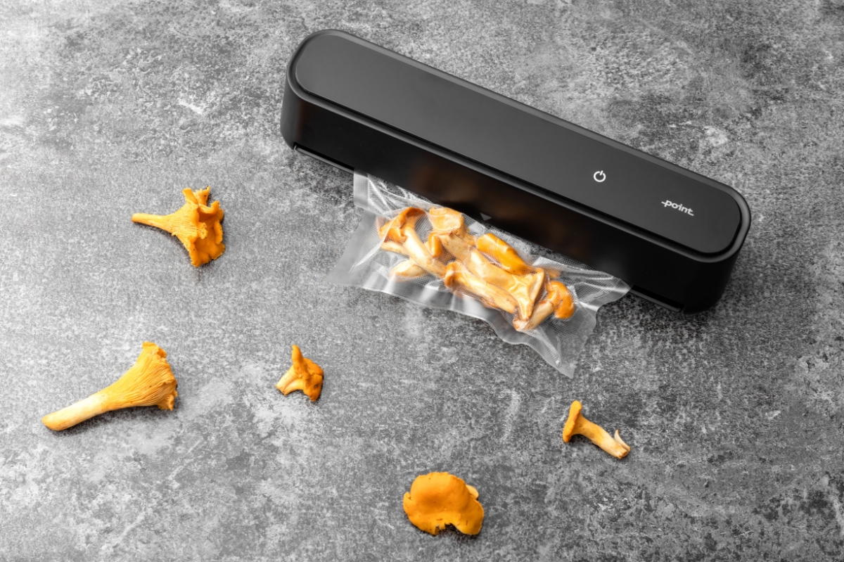 A picture of a black Point vacuum sealer on a marble table with a vacuum bag full of yellow chanterelles attached to the machine and chanterelles on the table also