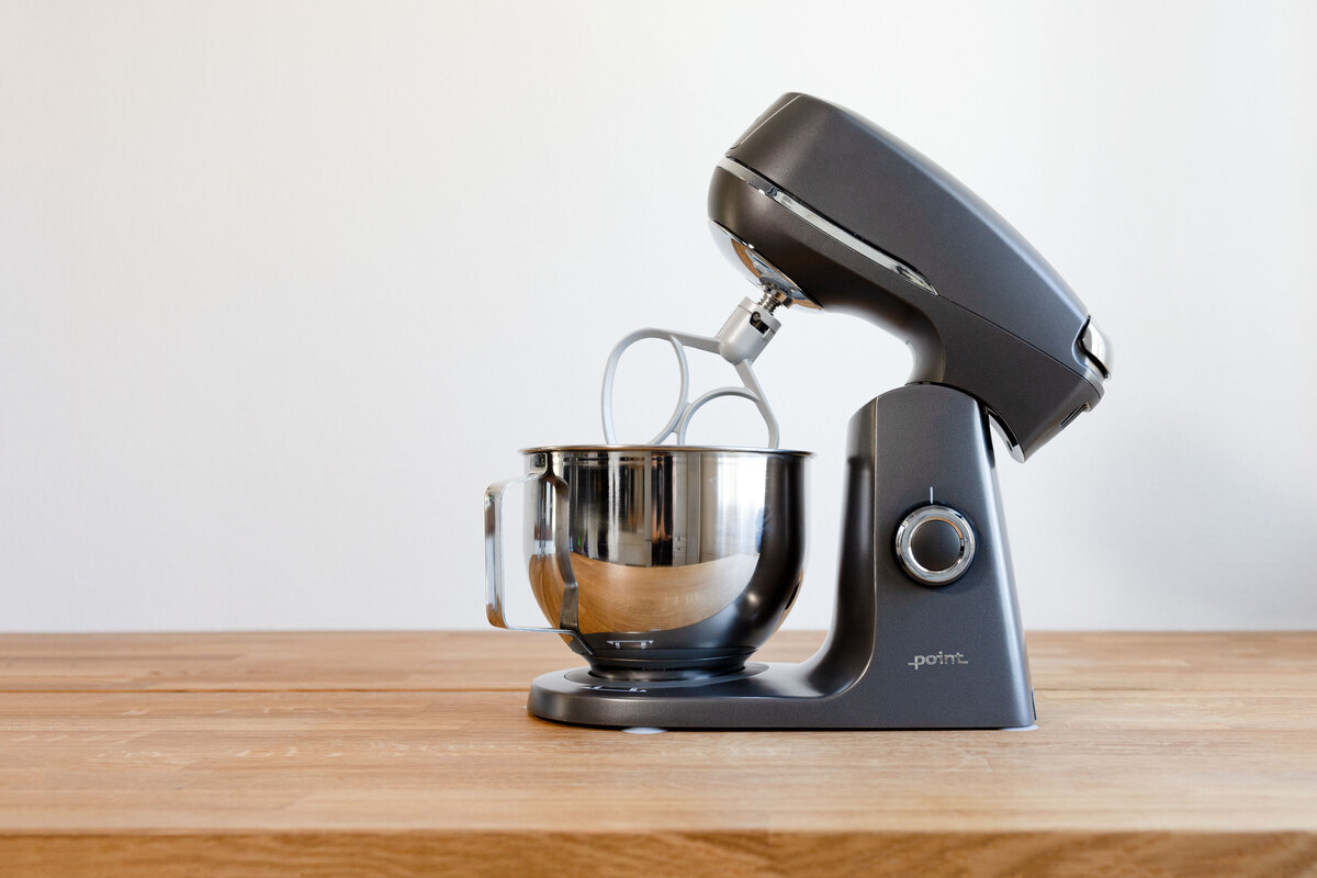 A picture of a grey kitchen machine on a wooden table with a whisk attached to it
