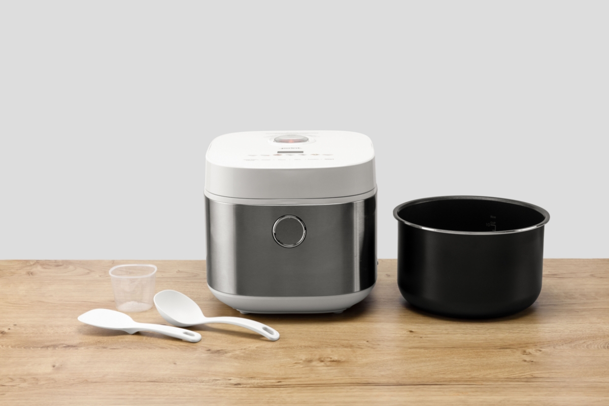 Wide angle image of POINT PORC5010 RICE/MULTI COOKER 5L on wooden countertop with its included accessories next to it.