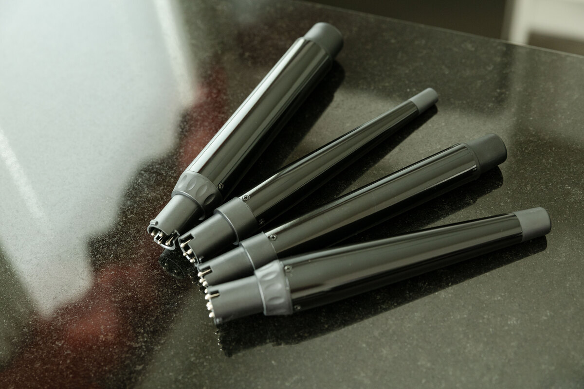 A close up of the four curling wands included in the package of Nooa Divine multi curler, two straight barrel shaped wands, and two tapered wands, on a dark surface